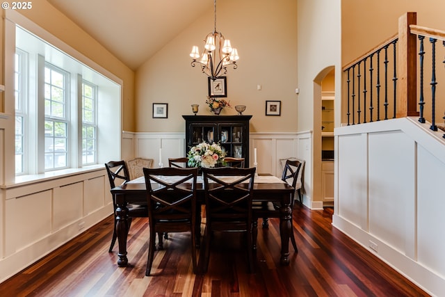 dining space featuring arched walkways, wainscoting, high vaulted ceiling, a decorative wall, and dark wood-type flooring
