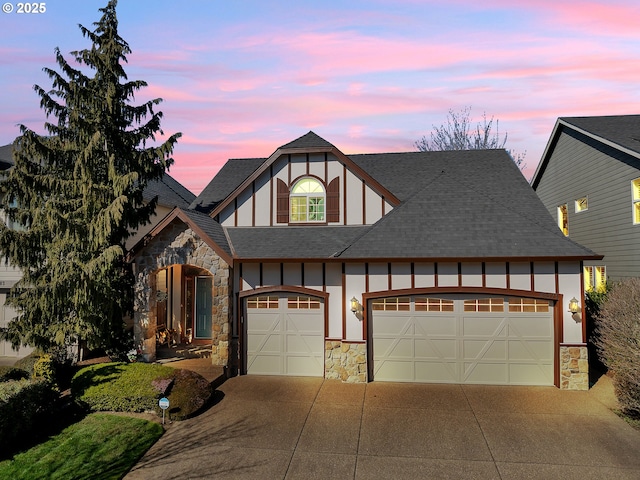 english style home with driveway, a garage, stone siding, and a shingled roof