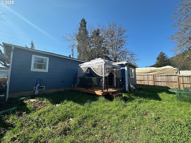 back of house with a deck, an outbuilding, fence, and a lawn