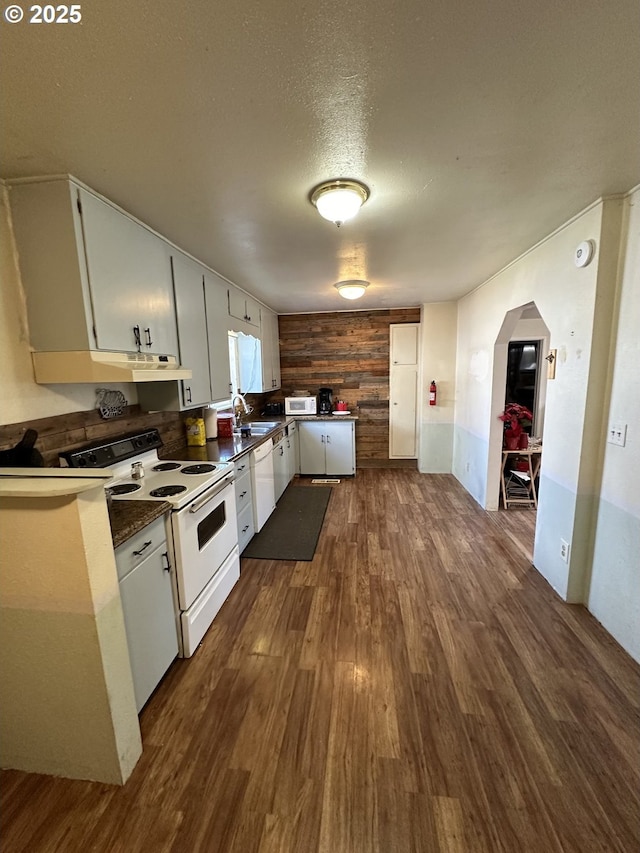 kitchen with under cabinet range hood, dark countertops, dark wood finished floors, white appliances, and arched walkways