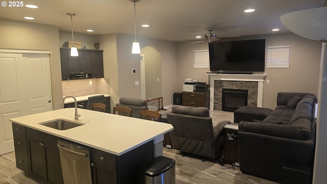 kitchen with dishwasher, a kitchen island with sink, sink, a fireplace, and decorative light fixtures