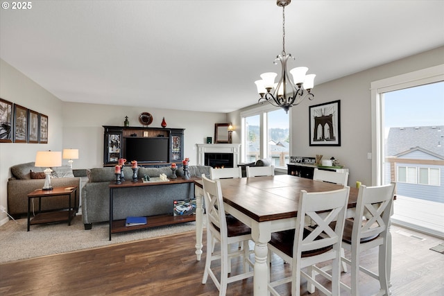dining room featuring a chandelier, wood finished floors, and a warm lit fireplace