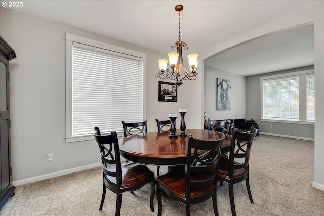 dining room featuring a chandelier, light carpet, baseboards, and arched walkways