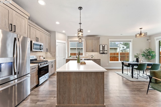 kitchen featuring wood finished floors, stainless steel appliances, decorative backsplash, light countertops, and a center island