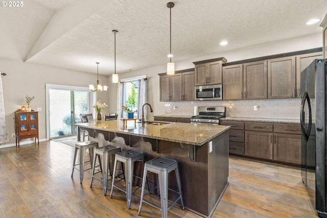 3276 S Mountain View Dr, Albany, OR 97322 - kitchen with stainless steel appliances, wood finished floors, decorative backsplash, an island with sink, and a chandelier