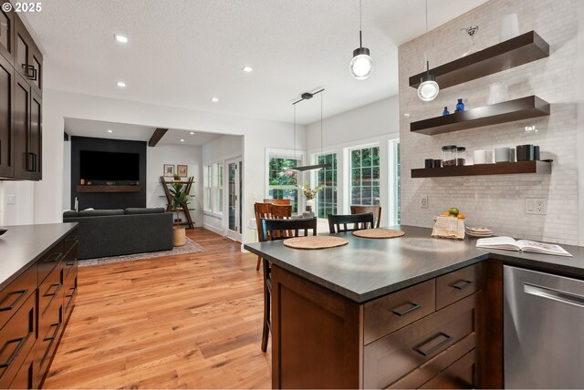 kitchen with stainless steel dishwasher, dark countertops, light wood-type flooring, backsplash, and hanging light fixtures