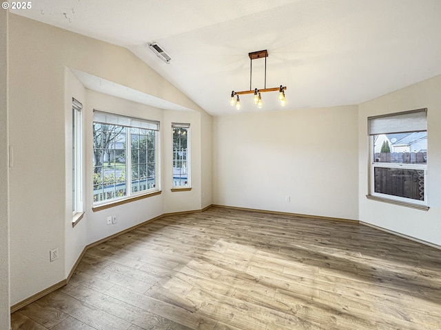 empty room with lofted ceiling, a notable chandelier, and light hardwood / wood-style flooring