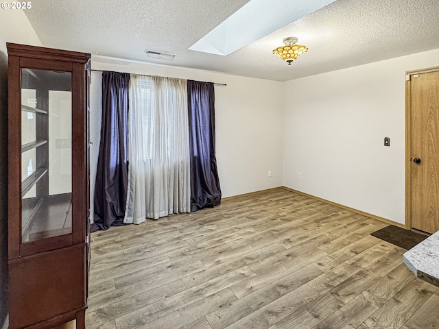 unfurnished room featuring light hardwood / wood-style floors, a skylight, and a textured ceiling