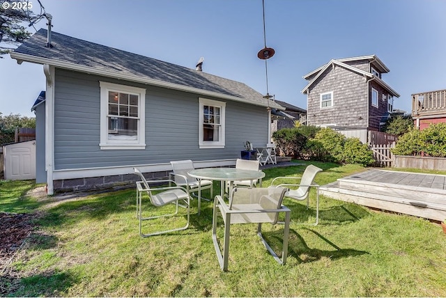 rear view of property with a shingled roof, a lawn, and a wooden deck