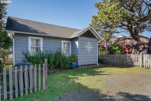 view of home's exterior featuring a shingled roof, fence, and a lawn