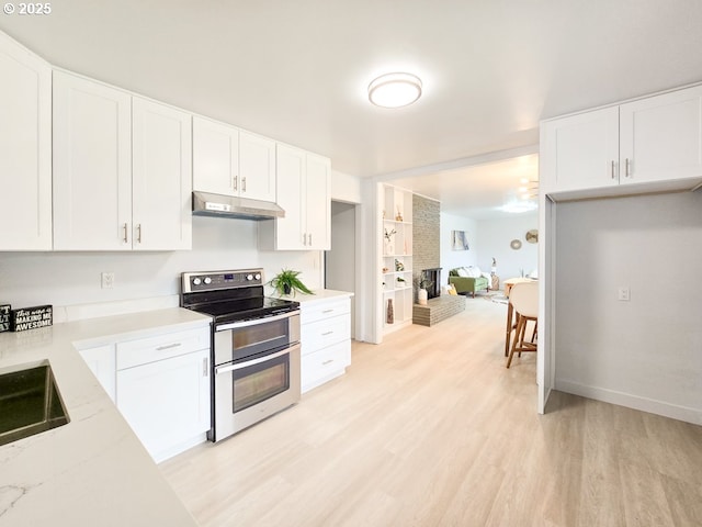 4145 SE Grant St, Portland, OR 97214 - kitchen with range with two ovens, under cabinet range hood, light wood-style flooring, a brick fireplace, and white cabinets