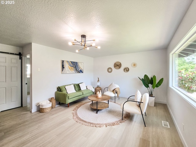 4145 SE Grant St, Portland, OR 97214 - living area featuring light wood-style flooring, a barn door, a chandelier, baseboards, and a textured ceiling