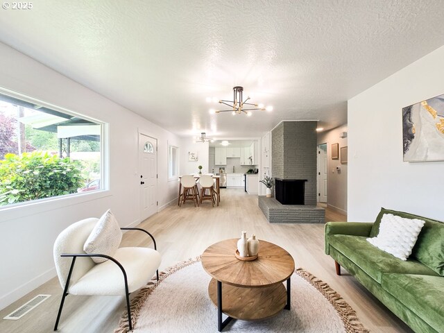 4145 SE Grant St, Portland, OR 97214 - living room with a chandelier, light wood-style flooring, baseboards, a textured ceiling, and a brick fireplace