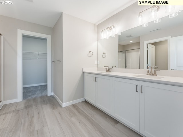 908 NW 178th Way, Ridgefield, WA 98642 - bathroom featuring a stall shower, wood finished floors, double vanity, a walk in closet, and baseboards
