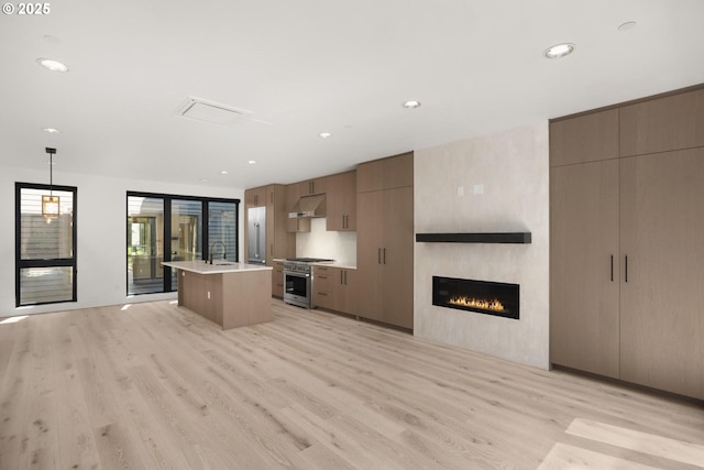 kitchen with pendant lighting, a fireplace, an island with sink, high end stainless steel range, and light hardwood / wood-style floors