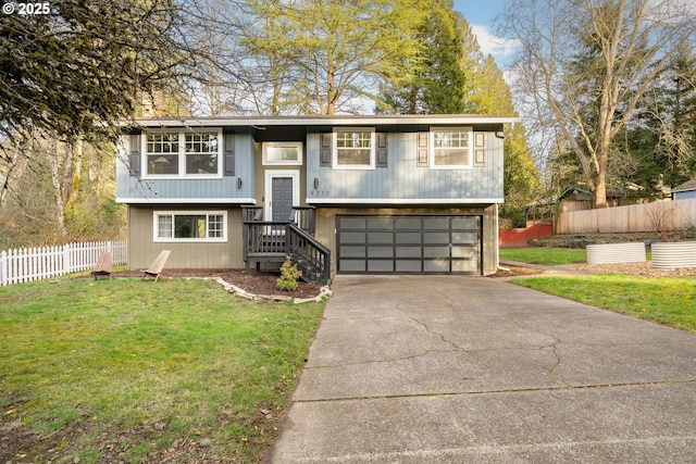 raised ranch featuring an attached garage, fence, a front lawn, and concrete driveway