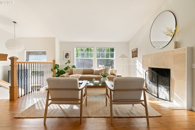 living room featuring light wood-type flooring, vaulted ceiling, and a tiled fireplace