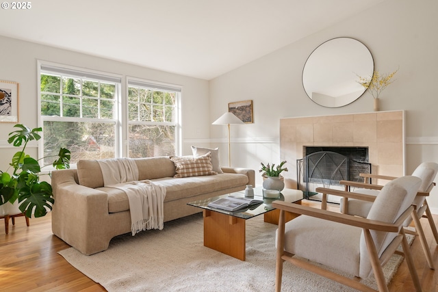 living area featuring vaulted ceiling, wainscoting, a tile fireplace, and light wood-style floors