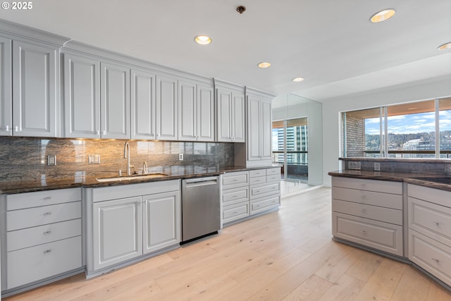 kitchen featuring dark stone counters, a sink, light wood-type flooring, dishwasher, and tasteful backsplash