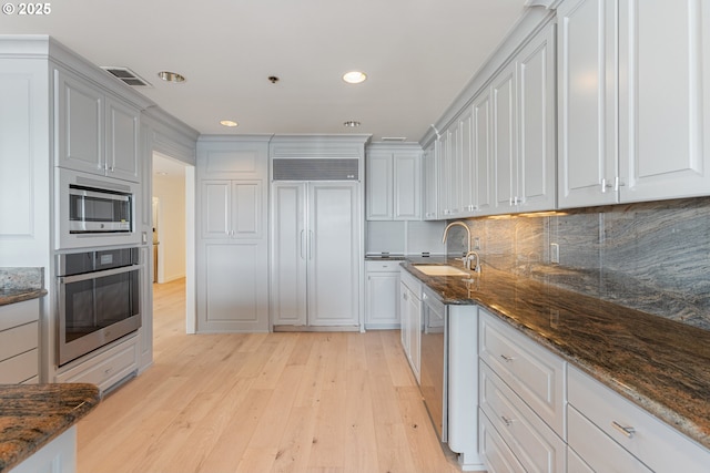 kitchen with visible vents, dark stone countertops, built in appliances, light wood-style floors, and backsplash