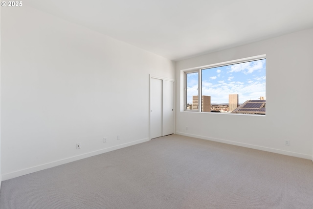 empty room featuring baseboards, a city view, and light colored carpet