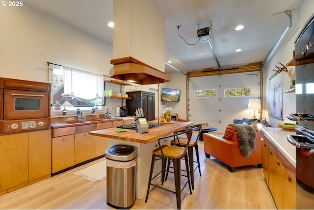 kitchen featuring a breakfast bar, stainless steel gas cooktop, butcher block countertops, and light hardwood / wood-style floors