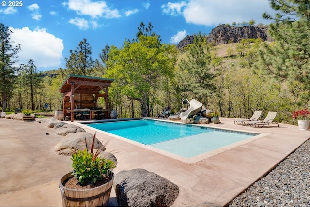 view of swimming pool featuring a gazebo, a water slide, a mountain view, and a patio area