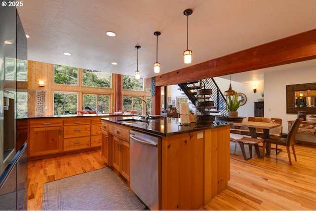 kitchen with pendant lighting, sink, dishwasher, an island with sink, and light wood-type flooring