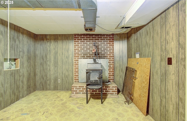 finished basement with a wood stove, wooden walls, and a paneled ceiling