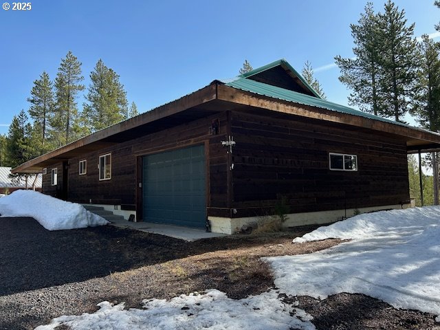 snow covered property featuring an attached garage and metal roof