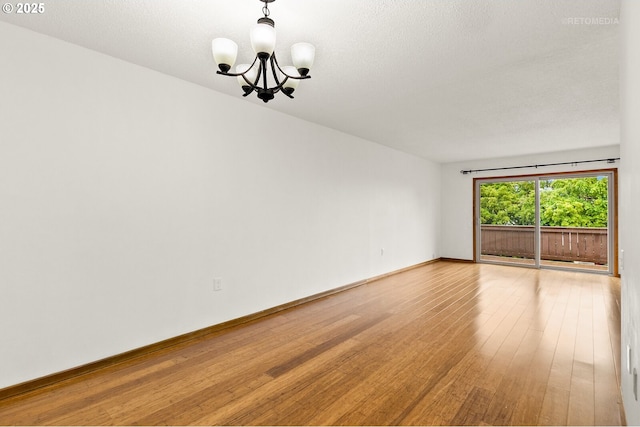 unfurnished room featuring a chandelier, hardwood / wood-style flooring, and baseboards