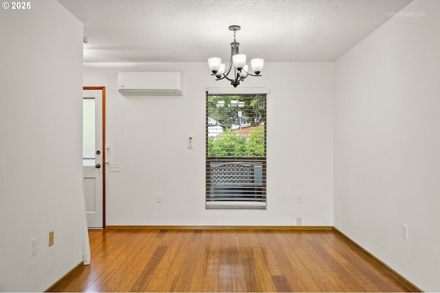 spare room with a wall mounted air conditioner, wood finished floors, a chandelier, baseboards, and a textured ceiling