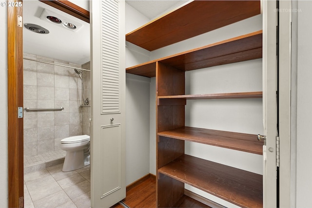 full bathroom featuring toilet, a tile shower, tile patterned flooring, and baseboards