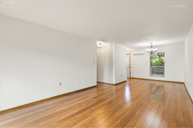 spare room with an AC wall unit, a chandelier, light wood-style flooring, and baseboards