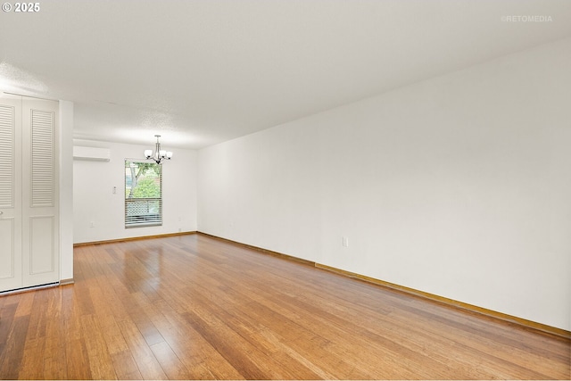 empty room featuring a chandelier, a wall mounted air conditioner, light wood finished floors, and baseboards