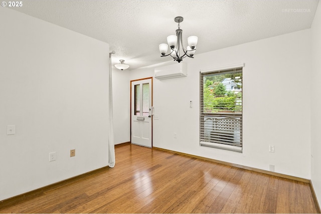 spare room with a wall mounted air conditioner, wood finished floors, a chandelier, a textured ceiling, and baseboards