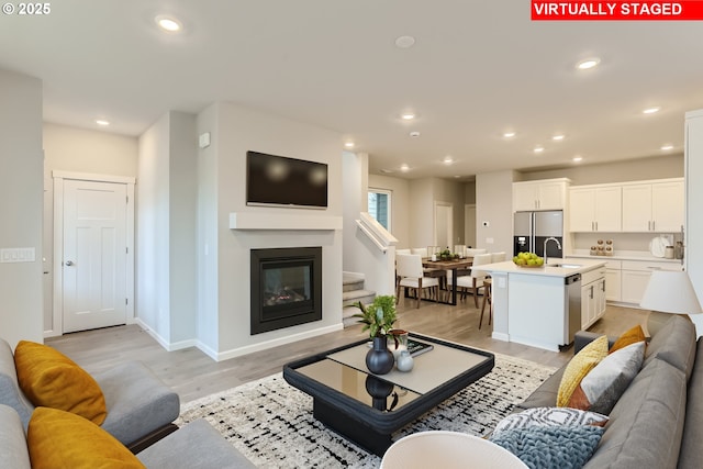 living room featuring baseboards, a glass covered fireplace, light wood-style flooring, stairs, and recessed lighting