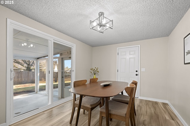 dining area with an inviting chandelier, a textured ceiling, and light hardwood / wood-style flooring