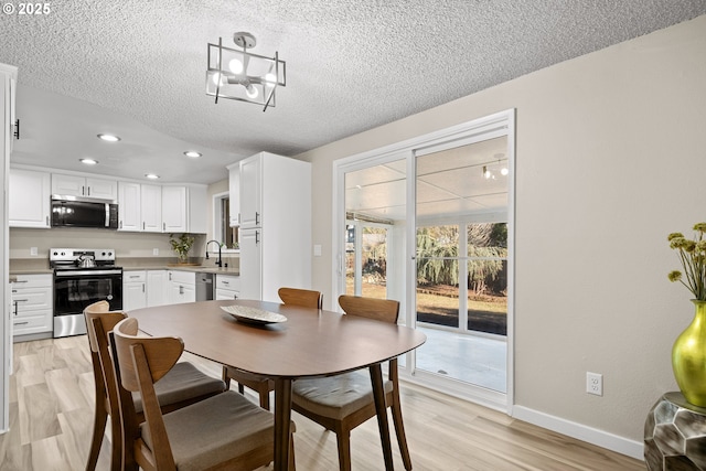 dining space featuring sink, an inviting chandelier, a textured ceiling, and light hardwood / wood-style flooring