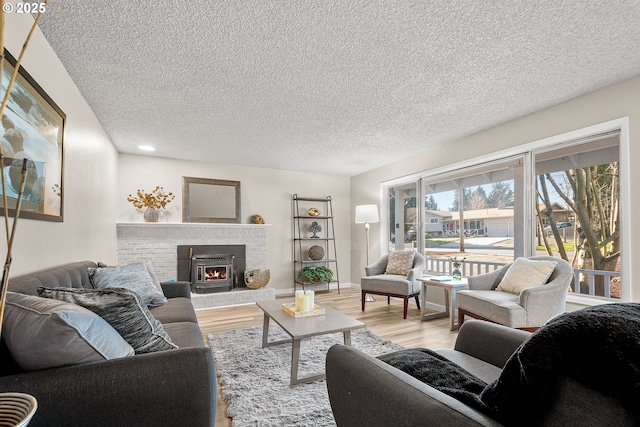 living room with a brick fireplace, a textured ceiling, and light hardwood / wood-style flooring