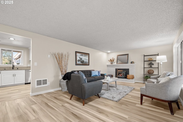 living room featuring light hardwood / wood-style floors, sink, a brick fireplace, and a textured ceiling