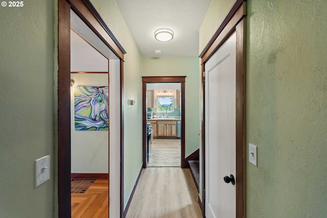 hall with light wood-style floors, baseboards, and a textured wall