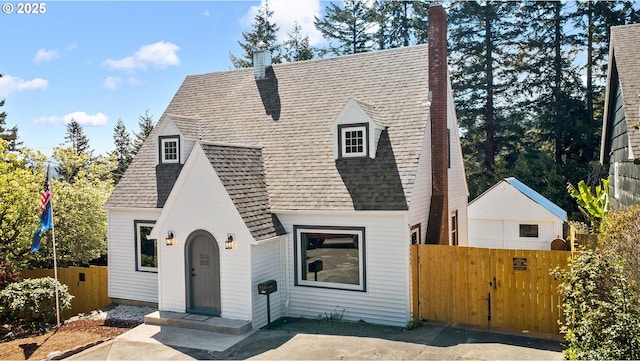 tudor house featuring a shingled roof, fence, and a chimney