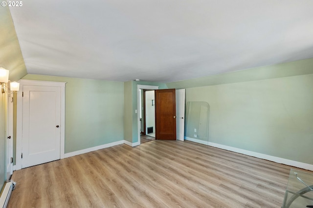 interior space with baseboards, light wood finished floors, lofted ceiling, and a baseboard heating unit