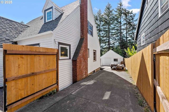 view of property exterior featuring a chimney, roof with shingles, a detached garage, fence, and an outdoor structure