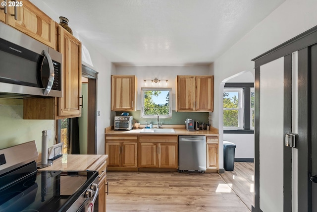 kitchen with arched walkways, light countertops, a sink, stainless steel appliances, and light wood-style flooring
