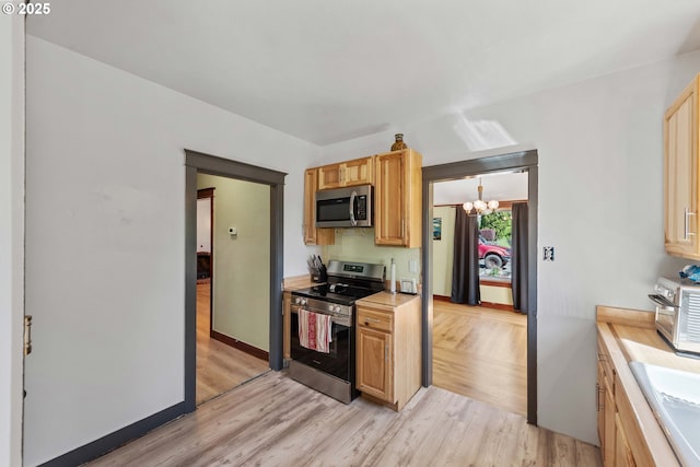 kitchen featuring light countertops, stainless steel appliances, a notable chandelier, and light wood-style floors