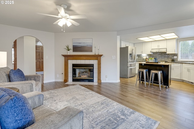 living room featuring light wood-type flooring, ceiling fan, and a tile fireplace