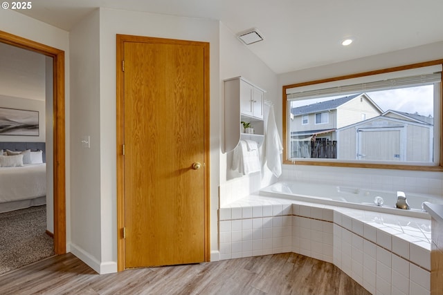 bathroom with wood-type flooring and tiled bath