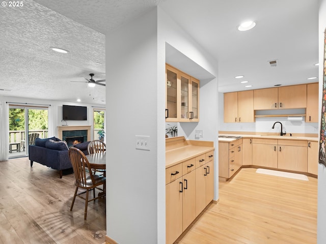 kitchen featuring light wood-type flooring, a tile fireplace, a sink, and light brown cabinetry